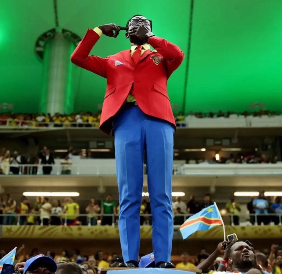 cnashr's tweet photo. Es bueno detenerse un momento en este gesto que se ha hecho viral en el mundial 2026 durante los partidos de la República Democrática del Congo. 

🎭 Él es Michel Nkuka Mboladinga (“Lumumba Vea”), conocido por imitar la estatua de Patrice Lumumba (1925-1961) quien fue líder independentista congoleño, panafricanista y el primer Primer Ministro de la República Democrática del Congo (RDC) tras la independencia de Bélgica, asesinado y hoy su figura es símbolo de la lucha por la soberanía y contra la explotación neocolonial.

🛑 El gesto de taparse la boca y poner los dedos en la sien es un símbolo de protesta usado por simpatizantes de la (RDC).

⛔️ Mano en la boca: Representa el silencio o el silenciamiento internacional ante las tragedias del país.
⛔️ Dedos/pistola en la sien: Simboliza la muerte, las ejecuciones, masacres y violencia armada que sufre la población congoleña. 

Esta es una denuncia contra el genocidio silencioso, las matanzas y la indiferencia global.