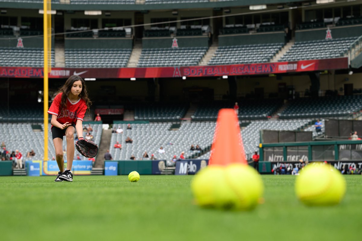 An Angels Softball Academy athlete reaches out their glove as they prepare to field a ground ball in the outfield grass at Angel Stadium. 