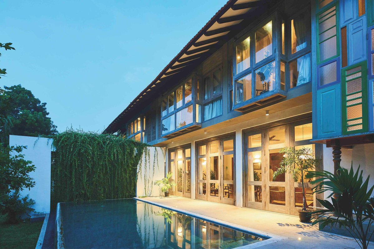 bt_options's tweet photo. Refurbishment of Navalar Villa, Nallur Jaffna

Designed by architects Chinthaka Wickramage and Shanthini Balasubramanium, Navalar Villa in Nallur draws inspiration from the vernacular architecture of the Jaffna Peninsula’s towns and villages, while celebrating the region’s rich cultural heritage.A dilapidated old manor house on the Jaffna peninsula, with warped roof beams, warped door windows, and many structural defects, was presented to the architects for refurbishment by clients who were returning to Sri Lanka after escaping to overseas due to the 25-year-old North East civil war in Sri Lanka.

The architects decided to replace all warped roof beams and door windows during the refurbishment, introducing cantilevered bay windows on the swimming pool side, a novel idea to create an interesting three-dimensional composition on the swimming pool side elevation, to be overlooked from the upper floor over the ground-floor veranda areas. Public areas of the villa are located centrally, while bedrooms are oriented to provide the best possible views of the swimming pool and rear garden.

This house asks how one lives an outdoor life. How does one work with the light, the wind, the environment, and foot traffic in a specific space? How do you frame the surrounding environment within the architecture? The outside environment is something you can almost feel, with the air passing through and it so immediate.

The house is unified by a double-pitched roof, supported by basic concrete and steel supports, and is composed of brick masonry walls and wooden, glazed wall planes, rendered seamless with painted plaster on the exterior. Glass-timber door windows become operable facades for controlling the interior climate, tuning with the long tropical monsoon and framing views of the rear garden.

The extended roof eave is carefully cantilevered to provide protection from the sun, wind, and rain.

In contrast upper floor is more private and intimate. Bedrooms provide spaces to sleep, rest, read and reflect. The upper floor is positioned in mutual tension with the guarantee of simultaneous intimacy and isolation so essential to the domestic interior.

The combination of materials and landscapes, along with the ‘thin’ section, facilitates cross-ventilation and allows the house to maintain its own cool microclimate in otherwise extreme hot and humid surroundings of the Jaffna Peninsula. Special architectural features of the villa include dark timber-columned verandas, white brick masonry walls, raised ‘thinnai plinths’ as built-in seats, and steeply sloping clay-tiled roofs. The garden is landscaped with lush green vegetation, using native trees and foliage. Decorative floral panels, held by a steel skeleton framework, were introduced to the car porch entry gable to celebrate the ‘sense of entry’ to the residence. Colorful recycled antique door and window panels, salvaged from old Jaffna houses, were introduced to the staircase cantilevered landing, overlooking the swimming pool side, as a feature wall. Raised podium ‘thinnai’ at the entrance veranda and under the staircase landing give a certain Jaffna vernacular flavor to the otherwise contemporary-styled Jaffna residence in Nallur, the Hindu religious cultural hub of the Jaffna peninsula.

The interior is tastefully furnished with easy chairs in the verandas and four-poster beds in the bedrooms. Alternatively, patterned triangular gable end panels were installed on the two gable ends of the long elevation, giving a contemporary modern aesthetic to the otherwise traditionally inclined residence, in line with the vernacular architectural idioms of the Jaffna peninsula. Special lighting design incorporating timber columns fixed ‘up and down lighting’ was introduced to supplement for the lack of originally available lighting fixtures of the residence. Existing cut cement floor which was in very bad state, was tiled over with pressed-cement tiles, maintaining the original residence interior ambiance. Calicut clay-tiled roofs, white-painted walls, dark timber columns, cement-handled ceiling soffits, and gray-washed doors and windows give a certain contemporary aesthetic to the otherwise traditional residence.