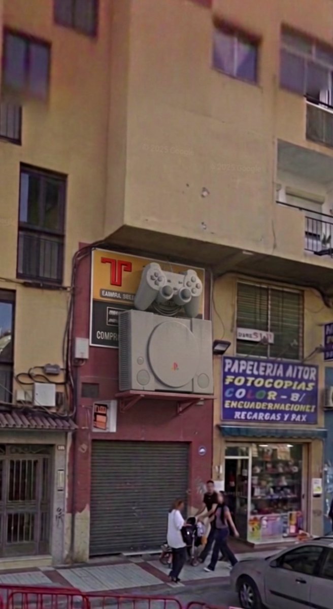 HuelinTV's tweet photo. Coleccionista retro en Instagram a la búsqueda de la PlayStation gigante que había en un local de calle Héroe de Sostoa en los 90. 
Imagen aproximada generada por IA, ya que no ha encontrado documento real: vía  https://t.co/MhMTXtt1ER https://t.co/rqJxWI8LFT