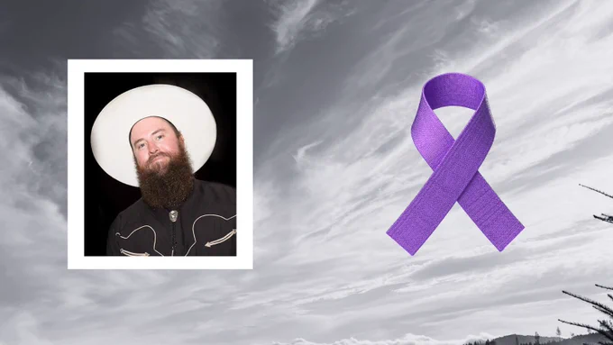 Man with a full beard wearing a white wide-brimmed hat and a black shirt against a dark background.