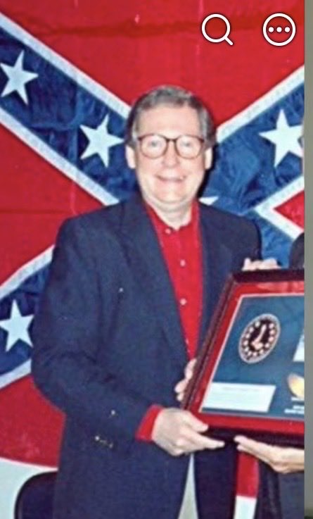 Suzierizzo1's tweet photo. Here’s an old pic of Mitch McConnell in the 1990’s standing and accepting an award in front of a Confederate flag. I think this pic tells us all we needed to know about Mitch. https://t.co/sw0a4RaRpP
