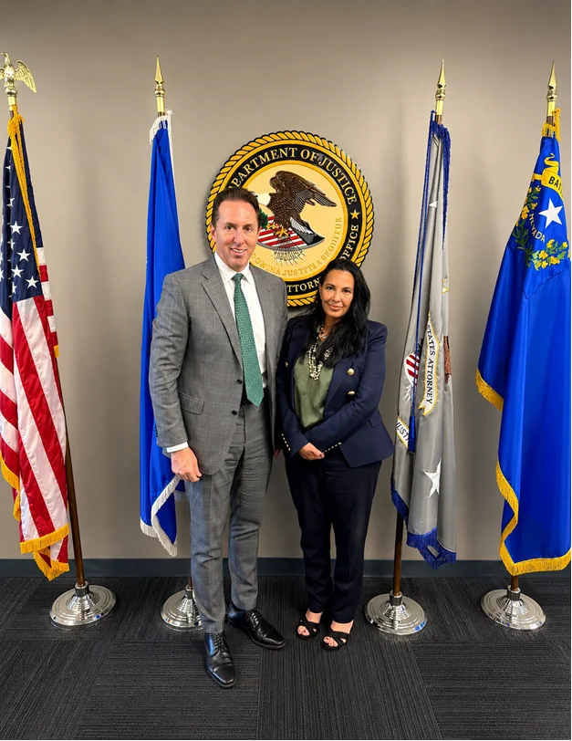 Photo of Deputy Secretary of Homeland Security Troy Edgar and First Assistant U.S. Attorney Sigal Chattah in front of U.S. Department of Justice seal and American, U.S. DOJ, State of Nevada flags.