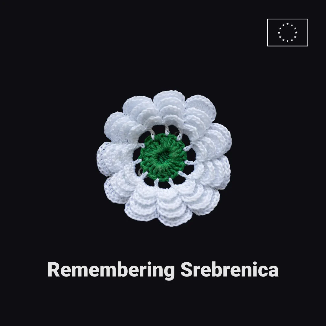 A white crocheted flower with a green centre on a black background. Below it is the text "Remembering Srebrenica". In the top right-hand corner is the EU flag. 
