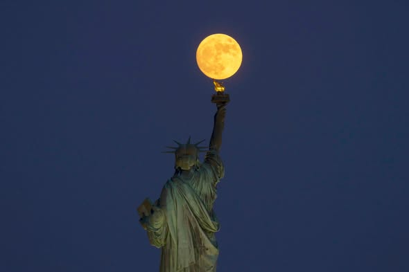 Chloe800000's tweet photo. The Strawberry Moon rises behind the Statue of Liberty as the sun sets in New York City, Sunday evening. https://t.co/oaXv9QDrS7