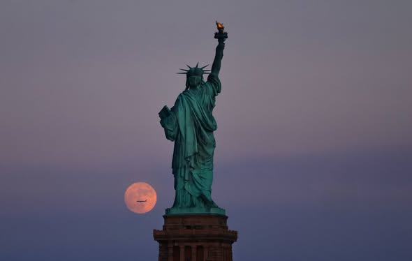Chloe800000's tweet photo. The Strawberry Moon rises behind the Statue of Liberty as the sun sets in New York City, Sunday evening. https://t.co/oaXv9QDrS7