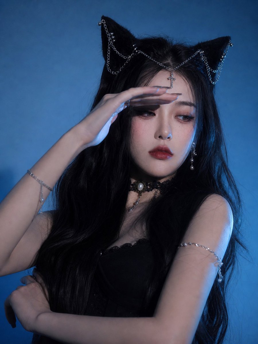 nanyuan0412's tweet photo. 上一篇我说，做系列图不要只写“换动作”。
这次前两张刚好很适合讲这个事。

第一张我让手抬到眉眼上方，像在挡冷光。
这个动作比“摸脸”“摸嘴唇”好用很多，因为它不是在卖萌，是在改变光线。
手一挡，眼睛就进入阴影。
人物的情绪立刻从“看我漂亮吗”变成“别烦我”。
猫耳和银链也顺便被推到画面上方，整个重心往头饰走。

第二张我反过来处理。
人物退远，靠墙，双臂抱住自己，旁边留一大片蓝色空白。
整体考留白撑起视觉语言。

很多时候我们做写真变体，会下意识把每张都拍得很满：脸要大，眼睛要清楚，饰品要全露，手还要有戏。
结果三张放一起，像同一个人坐在那里连续切了三个表情包。
变体真正该变的，不只是动作。
是画面的重心。

手在眉眼上方，重心往“光线和脸部阴影”走。
人物靠墙退远，重心往“空间和情绪”走。
同一套猫耳、银链、黑发、蓝背景都没变。
但第一张是冷光压过来。
第二张是她自己退到墙边。
这就够了。

做系列图的小经验：
别每张都让人物用脸硬撑。
有时候让手控制光。
有时候让留白控制情绪。
照片会比单纯换 pose 更像一套真正拍出来的片子。