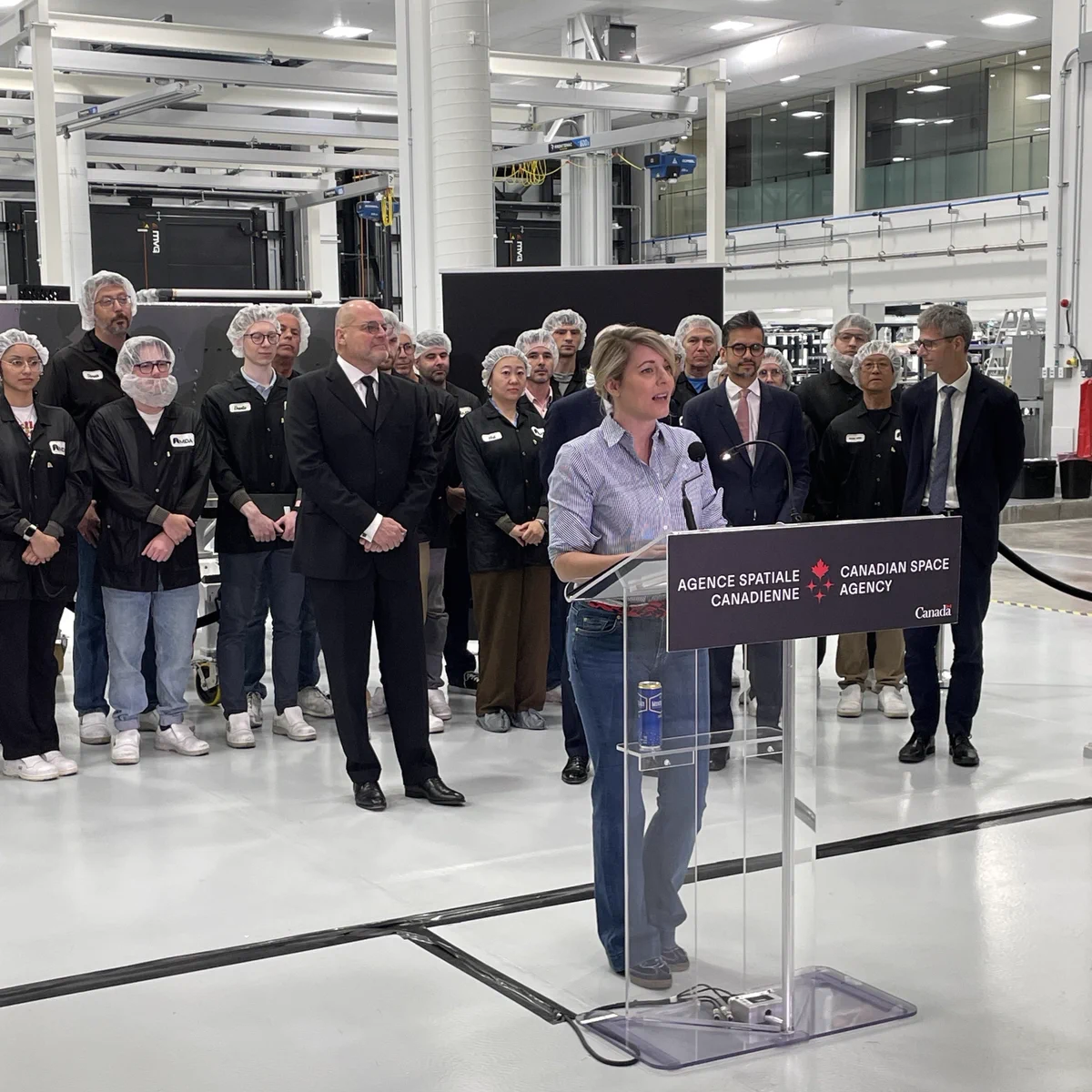 La ministre Joly s'exprime à un podium de l'Agence spatiale canadienne, avec des employés et des représentants officiels derrière elle.