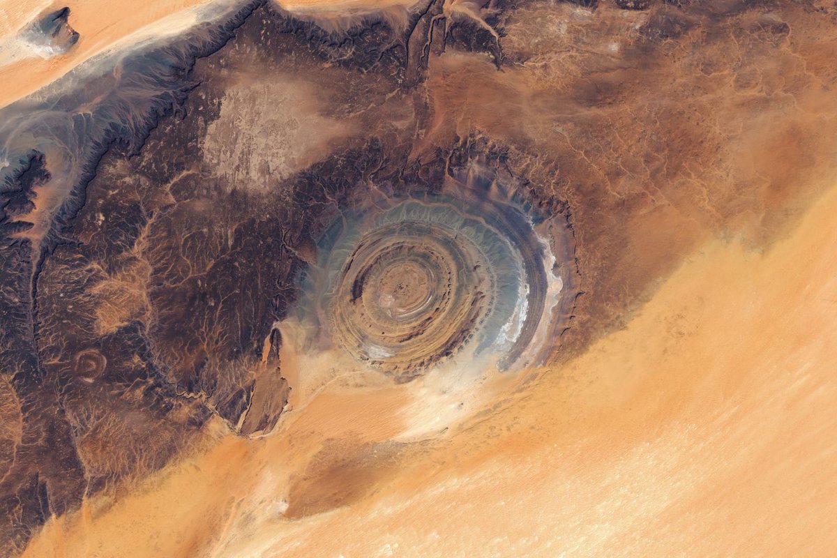 SETIInstitute's tweet photo. #PPOD: Eyeing the Richat Structure 👁️ 

In a remote part of northern #Mauritania, on the Adrar Plateau, lies a desert landscape that appears to be shaped primarily by natural forces. The region's most eye-catching feature when seen from above is the Richat Structure—a large geologic formation made of concentric ridges on the eastern side of the plateau. 

The 40-kilometer-wide structure was initially thought to be an impact crater. However, researchers later showed that it is actually a deeply eroded geologic dome formed by the uplift of rock above an underground igneous intrusion. Over time, differing erosion rates among rock types in the exposed upper dome led to the development of circular ridges known as cuestas. The orange and gray colors reflect differences in sedimentary and igneous rock types across the structure and the surrounding landscape. 

Credit: @NASAEarth Observatory/Lauren Dauphin 

#planetaryscience