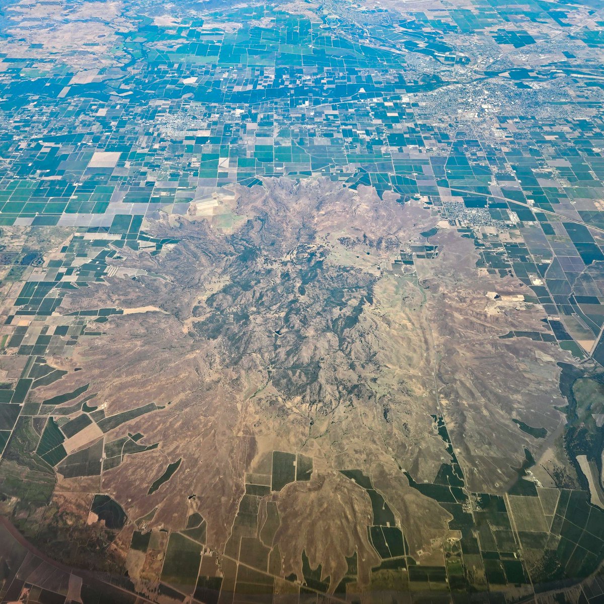USGSVolcanoes's tweet photo. California Volcano Observatory Weekly Update for June 29, 2026: All volcanoes in California were at normal background levels of activity for the last week. 

Is it a really overdone fried egg? A pancake? A flower? Nope, it's a volcano!

Sutter Buttes is the only volcano in California's Central Valley. Rising over 2,000 feet (610 m) over the valley floor, this enigmatic edifice was formed between 1.6 and 1.4 million years ago. Geologist James Dana described the cluster of hills as "an island in a vast prairie of millpond smoothness" when he first encountered Sutter Buttes in 1841, and the impression is certainly accurate. But what is a volcano doing so far away from any other volcanoes in California?

Instead of being part of the Cascade volcanic arc, like Lassen Peak and Mount Shasta, Sutter Buttes are related to the same Coast Range volcanic activity which formed the Clear Lake volcanic field. They may be related to a buried, inactive fault that separates the granitic and metamorphic rocks of the Sierra Nevada to the east, and the oceanic rocks of the Coast Range to the west. As shown by geophysical surveys, other faults intersect this deep, north-south-oriented crustal fault, possibly creating pathways for magma to ascend through the thick sedimentary rocks of the Central Valley. 

The eruptions that formed Sutter Buttes must have been a sight to see. The first magma to push through the sediments was sticky rhyolite, which formed thick, pasty domes and pyroclastic flows when explosions released trapped gas. After 30,000 years or so, bigger eruptions of andesite and dacite lava through multiple vents in the core of the volcano created even larger lava domes. They also warped the surrounding sedimentary rocks so much that their original horizontal layers became vertical or even overturned! During these eruptions, explosions and collapses formed pyroclastic flows, which flowed downslope and made a thick apron of debris all around the central domes. 

Though spectacular in appearance, Sutter Buttes isn't active anymore, and seems unlikely to ever be active again. It's simply a picturesque - and intriguing! - feature in California's Central Valley.

📷: This aerial photo, taken from about 40,000 feet and looking east, highlights the rugged central lava domes and smooth circular debris apron of the Sutter Buttes. (This photo has been edited to remove the airplane wing and window and enhanced for clarity.) USGS photo by J. Ball.

For the full text of this week's update, visit https://t.co/oQ7wo6WCDc

#USGS #CaliforniaVolcanoes #SutterButtes