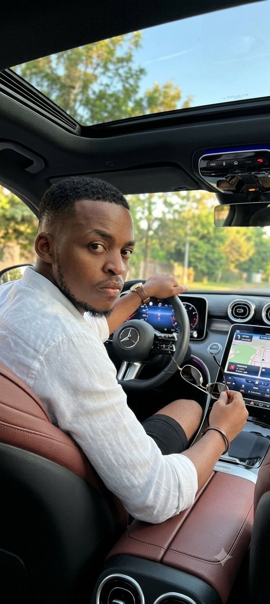 NjiwaFLow's tweet photo. 💨PICHA YA KUMTUMIA X WAKO😂

Weka Gemini hapo 😁

Use my selfie as the main reference and maintain 100% of my facial identity (face shape, hair, beard if any, skin tone and natural features). Do not alter my features.
Create an ultra-realistic image inside a modern luxury car.
Scene:
I am sitting in the driver's seat of a Mercedes-Benz C300 AMG, with interior trim in wine/coffee brown leather. The dashboard is modern with large digital screens, multimedia system playing music and active GPS.
Photo taken from the back seat of the car
The car has an open panoramic sunroof, showing blue sky and trees in the background.
Posture:
I am turned slightly towards the camera, serious and intimidating expression, holding the sports steering wheel with one hand and taking off my metal-framed aviator-style glasses with the other hand.
Clothing:
(white linen shirt with 3/4 button sleeves and black shorts), classic dark glasses, thin leather bracelet and coffee brown wristwatch
Lighting:
Natural light entering through the sunroof, sunny daytime weather.
Visual style:
Hyper-realistic photography, high definition, sharp details, realistic skin texture, natural appearance, no AI-like effects.
Ultra realistic photography, natural lighting, luxury lifestyle, high detail, sharp focus, realistic skin texture.