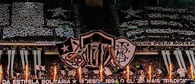 MovNacag's tweet photo. DESDE 1894

Quando Armando Albano, saudoso atleta do Botafogo Football Club, veio a falecer na sede do Mourisco Mar, dois homens tomaram talvez a maior decisão da história do Botafogo.

Augusto Frederico Schmidt, presidente do Club de Regatas Botafogo, e Eduardo Góis Trindade, presidente do Botafogo Football Club, protagonizaram um dos maiores símbolos de humildade e união que este clube já viu. Diante daquela tragédia, fizeram a pergunta que mudaria nossa história para sempre:

"O que mais é preciso para que os nossos dois clubes sejam um só?"

Desde então, nossa história passa a ter como marco inicial o dia 1º de julho de 1894. Nascemos na Praia de Botafogo, remando. E temos muito orgulho disso.

Mais do que o orgulho de sermos o clube poliesportivo relevante mais antigo do país, que esta data também seja sempre um momento de reflexão.

Schmidt e Eduardo abriram mão de suas vaidades e de seus projetos. Em meio à dor, entenderam que um Botafogo verdadeiramente unido seria muito mais forte.

Até meados de 2015 e 2016, porém, era incomum ver uma valorização do verdadeiro ano de fundação do Botafogo. Nosso centenário, por exemplo, foi comemorado em 2004, e não em 1994, como historicamente deveria ter sido.

Inconformados com isso, desde o primeiro coletivo que construímos, começamos a colocar 1894 em absolutamente tudo. Surgiram a Iniciativa Botafogo 1894, a Comissão de Festas 1894, o lendário estandarte escrito 1894 através dos Loucos Pelo Botafogo, diversas faixas com os dizeres "Desde 1894" e o maior bandeirão da história da nossa arquibancada, sempre com o mesmo padrão, o escudo do Club de Regatas à esquerda e o após fusão à direita. Até o apelido "O Mais Tradicional" ganha ainda mais sentido quando se compreende que o Botafogo é o clube poliesportivo mais antigo do país. 

Também é justo reconhecer o quanto a coleção de uniformes de 2019, especialmente a histórica camisa preta com o escudo do Club de Regatas, ajudou a popularizar essa visão da nossa história.

Somos o Botafogo de Futebol e Regatas.

Nascidos em 1894 para remar. E, depois, para transformar o Brasil no país do futebol.

📷 Luisa Portella e Vitor Silva