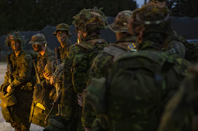 Soldiers in camouflage gear and helmets stand in formation during dusk.