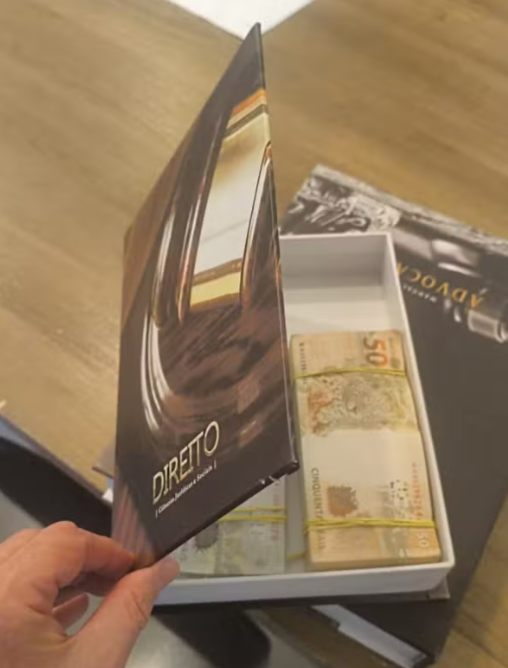 todandara's tweet photo. No clube do livro da direita, ninguém debate a obra, só confere se tem dinheiro dentro. Aliados do líder do PL, Sóstenes Cavalcantes, do partido de Flávio Bolsonaro, foram alvos da PF por suspeita de desvio de cota parlamentar e até dinheiro em LIVRO FALSO apareceu. Depois querem dar aula de moralidade. A casa caiu!