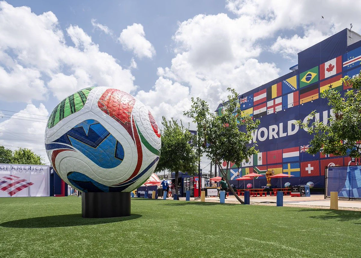 Photograph of a soccer ball sculpture. In the background is part of a World Cup venue that is decorated with flags from various countries. Credit: NASA/Luna Posadas Nava
