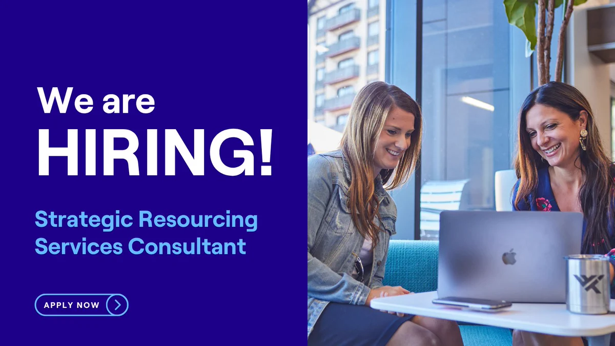 We are HIRING! Strategic Resourcing Services Consultant. APPLY NOW. Two smiling women look at a laptop on a table in an office. One wears a denim jacket, the other a patterned top. A phone & branded mug are nearby.