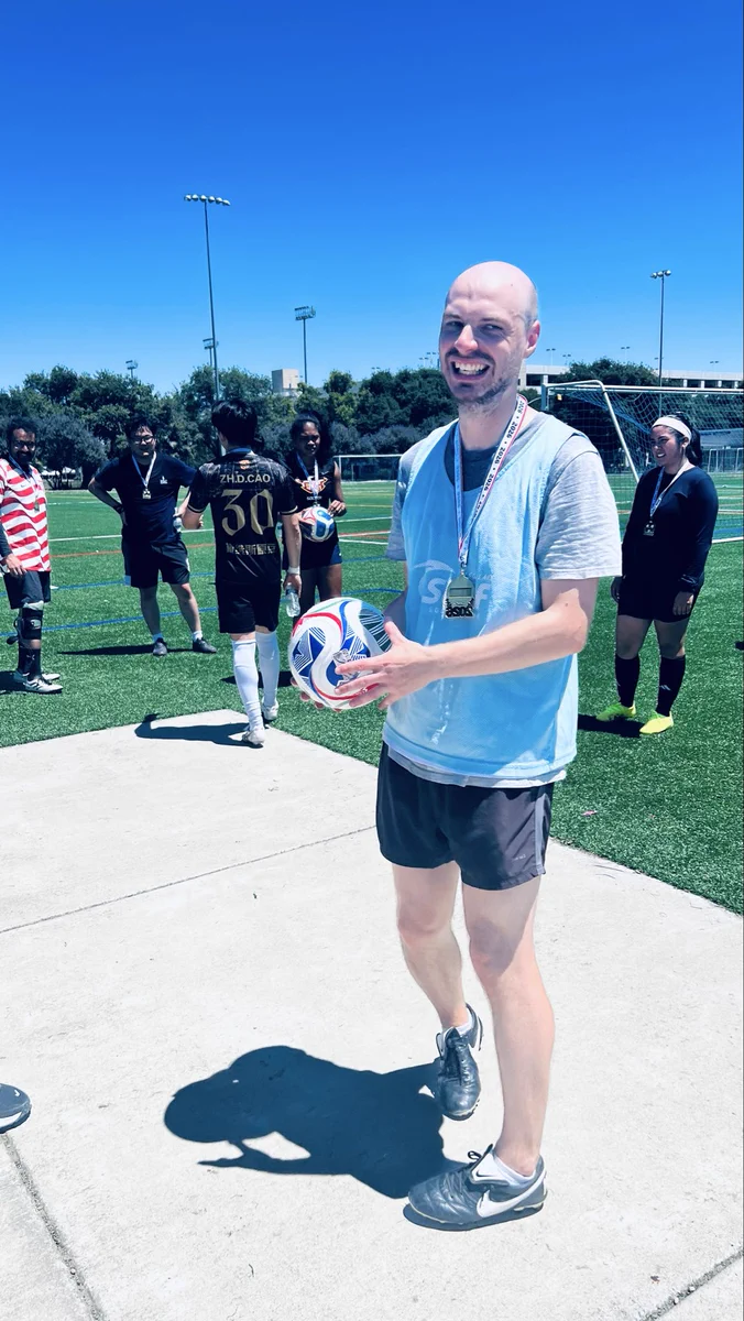 Grad student smiling while holding soccer ball and wearing a blue jersey.