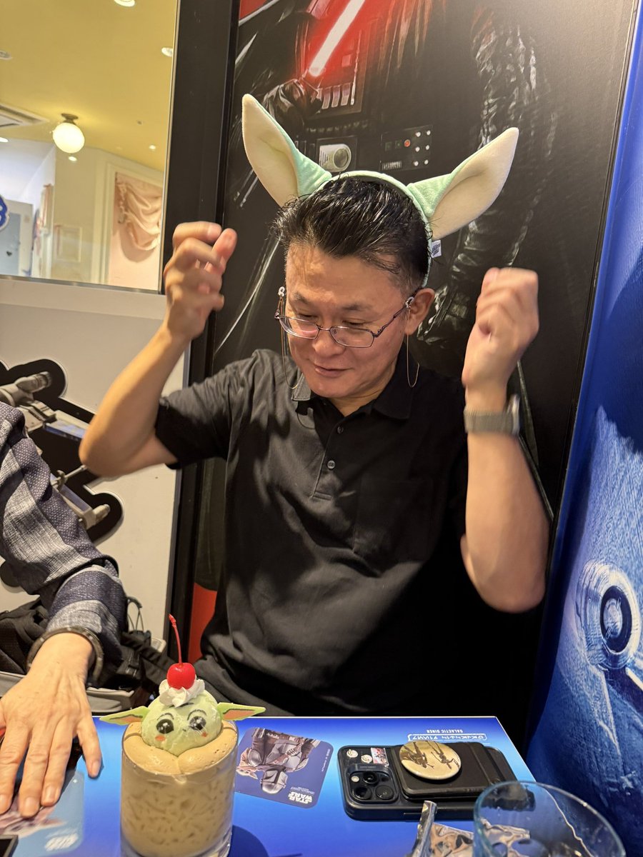 XnP1v's tweet photo. 絵本『マンダロリアンとグローグー』企画編集担当です。

終日、予約で満席が続くスター・ウォーズカフェ（渋谷）に行ってきました。目的は視察と新企画の打ち合わせ。客層は女性客8割くらい。もうこれだけでも目からウロコの感動ものです。SWといえばメンズの牙城的なイメージがまったくないんです。

それで、Aさんが持ってこられたグローグーカチューシャをかぶらせてもらいました。カチューシャなんて初めてつけました。えっと、あのー、ちゃんと打ち合わせしてるんです、これでも(^^)

日本で千客万来となっている新装SWフランチャイズは、グローグーのおかげで新たな「出会い」と「ご縁」の場所を次々と生み出しています。９月から始まると噂されている壮大な常設POPUPストアも実現したらすごいことになりそうですね。

女性ファンにも愛されるスター・ウォーズカルチャー。想像が現実になってきて、より裾野を広げた新企画や商品開発に、がぜん力が入ってきます。
