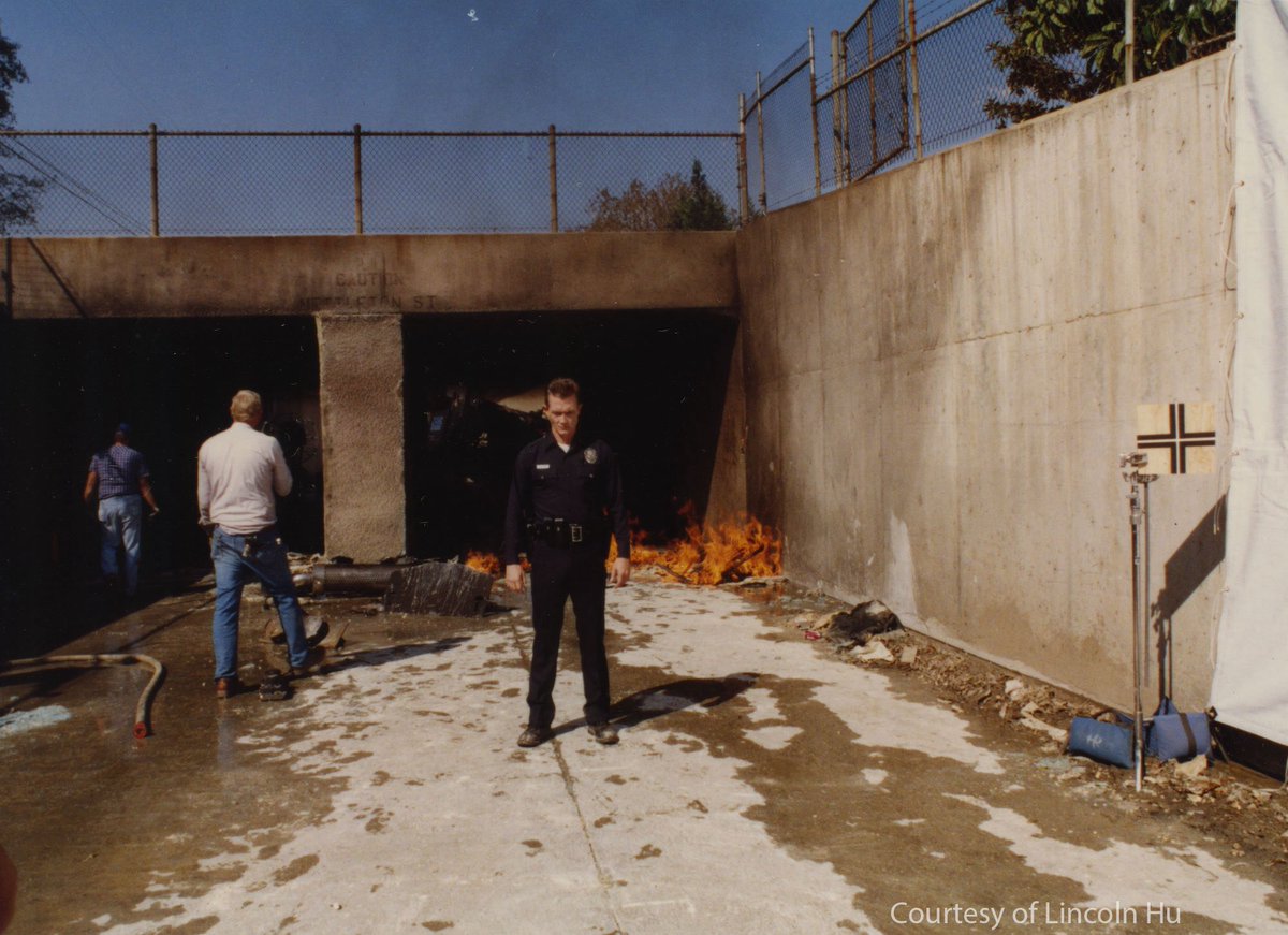 ILMVFX's tweet photo. During production of Terminator 2: Judgment Day–now celebrating its 35th anniversary–the ILM CG crew shot plate reference photography on location with director James Cameron and the live action team. CG shot supervisor Lincoln Hu generously shared these images from his personal archives, which he snapped while some of T2's most iconic moments were being filmed. It was up to Lincoln and his ILM colleagues to bring the digital T-1000 character to life within these live action shots. Among the ILM team were visual effects supervisor Dennis Muren, assistant visual effects supervisor Mark Dippé, and CG animation supervisor Steve Williams, seen here alongside Hu in an early "selfie" shot in the reflection of their chrome sphere.