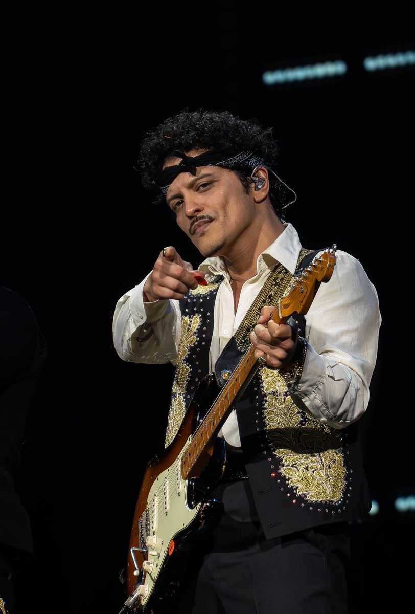 BrunoMarsAccess's tweet photo. “No primeiro show em Amsterdam, Bruno Mars provou mais uma vez que é um dos maiores entertainers da música pop contemporânea.

É preciso ter coragem para abrir um show em estádio com uma balada. Bruno Mars faz isso, e funciona. Risk It All, uma açucarada canção de amor com influência latina, serve como a proverbial calmaria antes da tempestade. Logo após seu fim, um verdadeiro espetáculo toma conta do palco. Durante duas horas e quinze minutos, Bruno Mars domina a apresentação e, com exceção de algumas músicas ao piano, o ritmo permanece acelerado e a energia, contagiante.

The Romantic é, em parte, uma homenagem à cultura chicana e latina. Embora isso talvez não seja evidente à primeira vista, o cantor, nascido e criado no Havaí, também tem ascendência porto-riquenha. Na Arena, trompetes de mariachi dividem espaço com um rock latino que remete ao som de Santana nos anos 1970. E quando Mars assume as congas, o gênio musical mostra que também domina esse instrumento com maestria.

O público permanece eufórico durante toda a noite, e com razão. Basta Mars balançar um braço para que a Arena se transforme em uma floresta de mãos agitadas. E quando ele ordena “jump, jump”, o estádio inteiro começa a pular, fazendo por um instante você se perguntar se a estrutura suporta tamanha força.“ — Het Parool em critica sobre a The Romantic Tour.