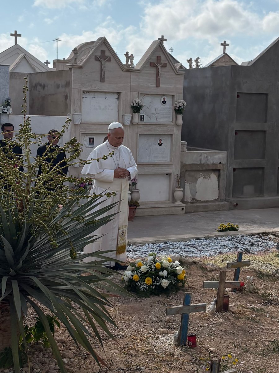 vaticannews_it's tweet photo. Il #Papa è a #Lampedusa. E inizia la visita con una preghiera silenziosa al Cimitero di cala pisana dinanzi alle croci di legno dei migranti, tra cui quella del piccolo Yusuf morto a 6 mesi in un naufragio nel 2020. #LeoneXIV depone una corona di fiori.

#visitapastorale https://t.co/cEAD4wPYET