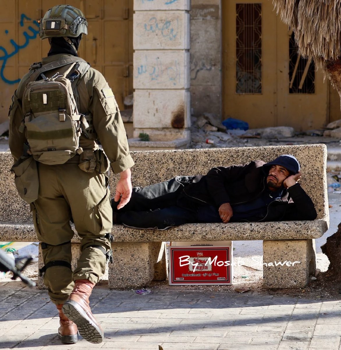 EyeonPalestine's tweet photo. A Palestinian lies casually on a bench in defiance of Israeli occupation soldiers during their raid on Hebron’s Old City, carried out to secure the entry of Israeli settlers into the area. https://t.co/GANdmSOnmH