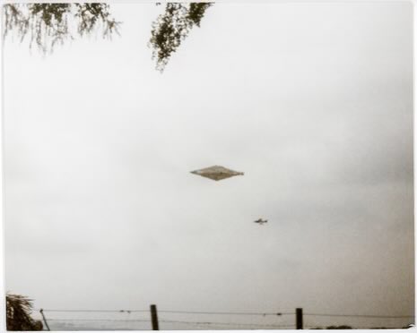Only_Ryan02's tweet photo. The Calvine photo was taken in August 1990 near Calvine, Scotland, by a hotel chef who, along with a colleague, witnessed a large diamond-shaped object in the sky. 

He captured the image showing the metallic, lozenge-like craft hovering above the rural landscape with power lines and trees in the foreground, and a smaller aircraft (possibly a Harrier jet) nearby. 

The negatives were later turned over to the UK Ministry of Defence before the photo was leaked publicly.

Researcher @jamescfox also visited the Calvine site and confirmed no nearby body of water exists, ruling out any  rock skipping off the water, or reflection theory.