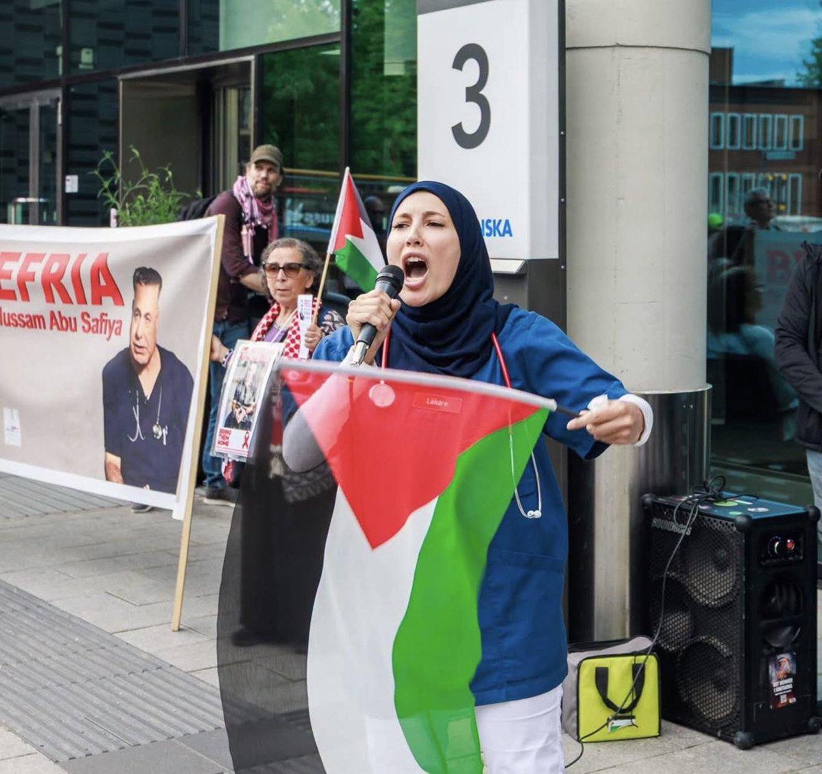 svennbenn's tweet photo. Läkaren Zainab skanderar sitt stöd för dr Abu Safiya utanför Karolinska, iförd sjukhusets kläder.

Hon använder sin tjänst och Karolinskas faciliteter för att legitimer sin ståndpunkt, precis som Hamas gör. Det råkar vara så att den gripna Safiya även är Hamasgeneral. https://t.co/TBkyYOuyn3