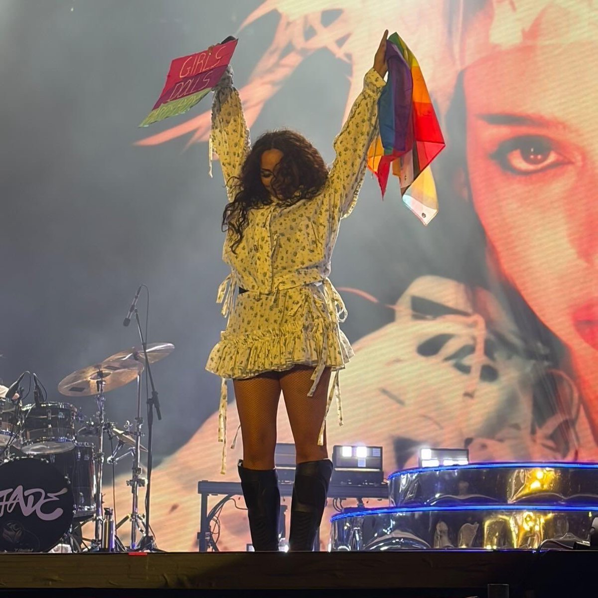 JADEtearoom's tweet photo. JADE holds up a Pride flag and a “GIRLS, DOLLS, PARTY BOYS” sign from fans while performing her LGBTQ+ anthem ‘Church’ in Poland, where same-sex marriage is banned, no specific hate crime laws exist to protect LGBTQ+ people, and “LGBT Ideology Free Zones” were only abolished in 2025 due to severe retaliatory funding cuts from the EU