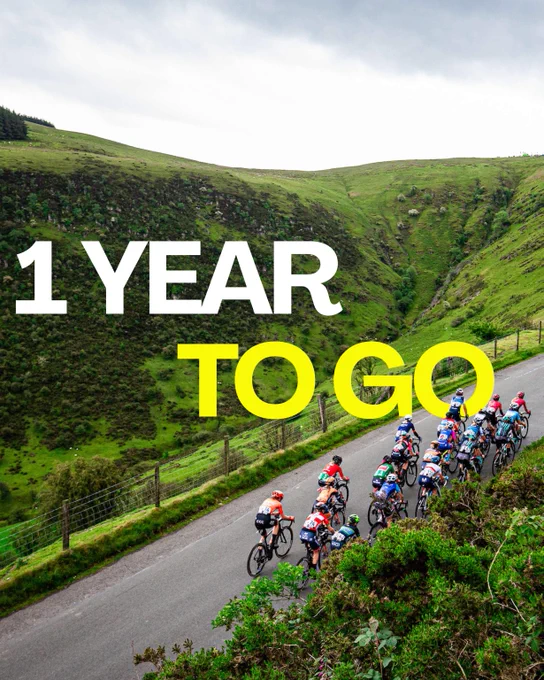 1 YEAR TO GO” graphic over an image of cyclists riding along a winding road through green Welsh hills.
