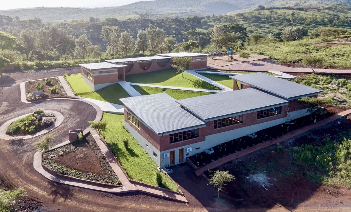 shavnyuyngah's tweet photo. When we build for our environment it directly suits our needs. This school is a clear example of what a typical school on this continent should look like.

Black Rhino Academy in Karatu, Tanzania sits at the edge of the Ngorongoro Crater, designed by NLÉ, the architecture firm led by Kunlé Adeyemi. The entire campus is built from locally made earth bricks, formed into catenary arches by hanging a chain under its own weight, reversing the curve, and using it as the natural line of compression. No complex engineering software. Physics and brick. The arches expand and contract across the uneven landscape, adapting to every slope, connecting classrooms and retaining walls into one continuous flowing structure. The masterplan is drawn directly from the Iraqw and Masai Boma settlement pattern, protective rings of clustered buildings organized around shared open space.

Grass. Plants. Brick. Open air corridors. The temperatures inside these classrooms will always be balanced because the building was designed for this climate, not borrowed from a catalogue meant for a different one. The ventilation is natural, which means fewer fans pushing recycled air into lungs and fewer children with chronic catarrh and coughs that disrupt their ability to focus and learn. The research on thermal comfort and learning performance is clear: children learn better when they are not overheated and uncomfortable.

Now compare this to the white cement boxes with tiny windows we paint and pretend are schools. The white boxes should be banned from this continent. This is the standard. Brick, catenary arch, open courtyard, grass underfoot and the landscape as part of the curriculum.

Karatu, Tanzania | NLÉ, Kunlé Adeyemi | Completed 2018