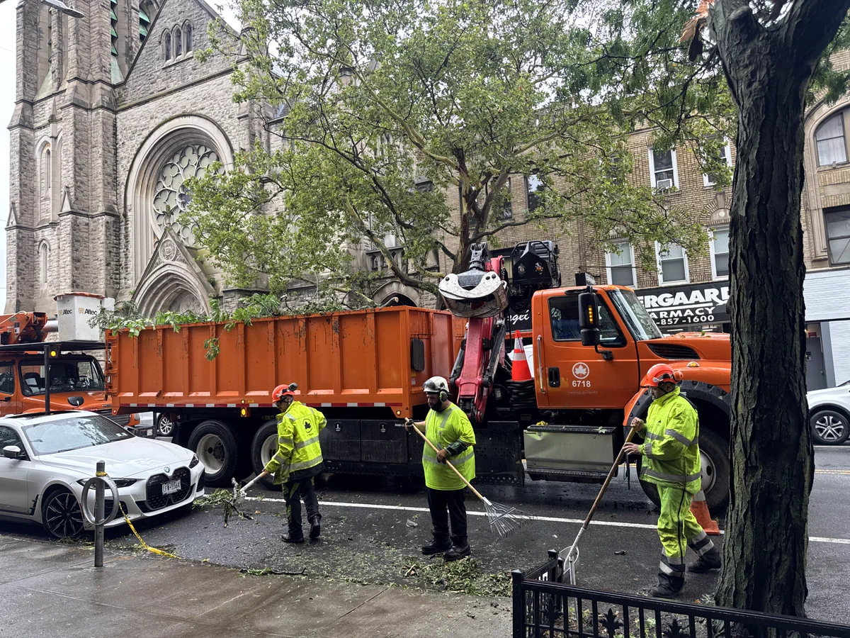 Three Parks workers stand beside an orange truck raking leaves! 