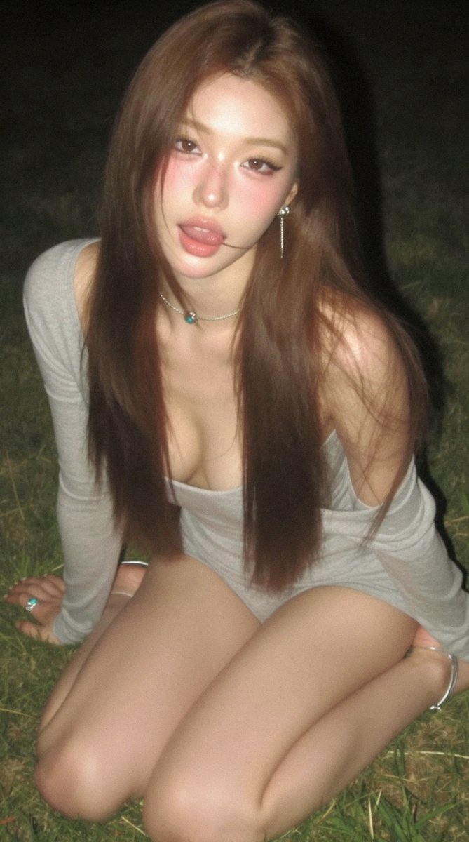 ailiabot's tweet photo. prompt：⬇️

A captivating young East Asian woman kneels on a nighttime grass field, her long silky straight brown hair with a natural center part cascading over her shoulders and chest, one delicate strand lightly resting against the corner of her mouth. Her skin is porcelain-smooth and dewy with strong luminous highlights, cheeks flushed with soft natural pink blush. She has exquisitely refined features: large expressive eyes enhanced with bold eyeliner and thick lashes gazing directly at the camera with an alluring expression, a petite delicate nose, and full plump lips coated in glossy pink lip gloss, slightly parted as her tongue tip gently presses against the lower lip, conveying a perfect mix of cute innocence and seduction. She wears a light gray off-shoulder long-sleeve tight knit romper, the wide neckline slipped down to reveal smooth bare shoulders and deep cleavage, the lightweight fabric clinging to her curves with natural soft folds and creases, the short hem exposing her thighs. Her pose is intimate and relaxed — knees pressed together as she sits back on her heels, both hands planted on the grass in front for support, upper body leaning slightly forward. She wears a thin silver necklace with a round turquoise pendant resting on her collarbone, long dangling silver tassel earrings, small rings on her fingers, and a slim silver anklet on one ankle. The scene is an outdoor nighttime grass lawn surrounded by lush green grass blades and a dark softly blurred background. Low-angle close-up composition places her as the dominant subject filling most of the frame, with the background gently defocused to create strong intimacy and visual focus. Soft nighttime side lighting and ambient glow illuminate her form, producing realistic highlights, gentle shadows, and luminous reflections across her dewy skin and silky hair for a cinematic night atmosphere. Photorealistic cinematic night photography style with extreme fine details: natural skin texture with visible pores and dewy sheen, individual hair strands with lifelike movement and shine, authentic knit fabric texture and folds on the clothing, crisp grass details. The color palette balances cool nocturnal tones with warm skin tones and muted gray fabric, resulting in a mysterious, intimate, and story-rich mood.