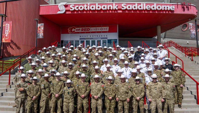 Large group of military personnel in uniform and white cowboy hats posing on steps outside the Scotiabank Saddledome