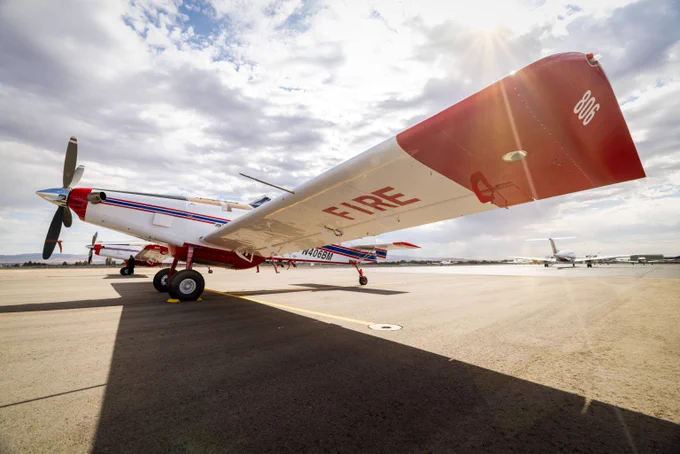 Red and white firefighting airplane parked on a sunny airport tarmac under a partly cloudy sky.