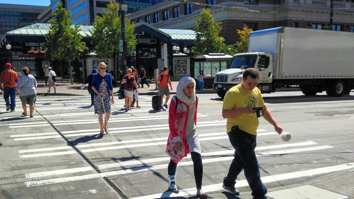 People cross the street in front of King St Station. One is vision impaired and using a cane.