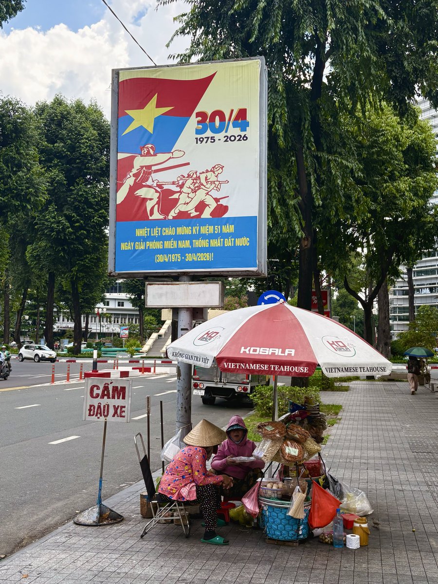 Iwashereyt's tweet photo. 📍 Ho Chi Minh/Saigon 🇻🇳

Everyday life beneath Vietnam’s history. Street vendors sit below a billboard commemorating the 51st anniversary of reunification (30 April 1975–2026)

#HoChiMinh #Saigon #Vietnam #streetphotography #asiatravel https://t.co/KRWh8H7pQo