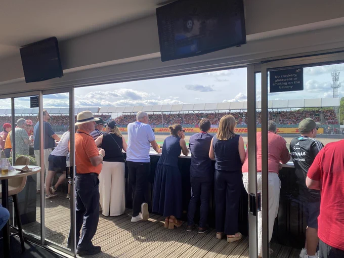 Yardi clients are gathered in a lounge area overlooking a racetrack, with a crowd in the stands on the opposite side. 