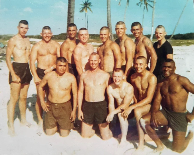 Thirteen men lined up on the beach (eight standing in the back row, five kneeling in the front) comprise "Team Broadminded."