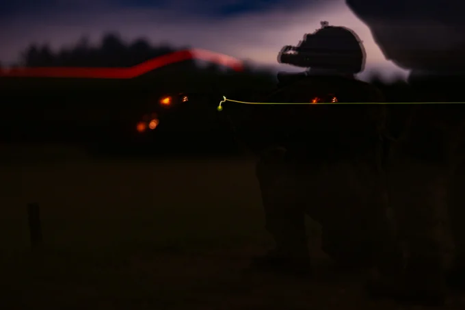 Soldier in tactical gear firing a weapon at night.