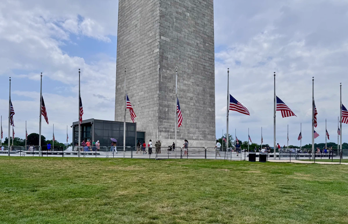 A large stone monument is surrounded by flags being flown at half staff.
