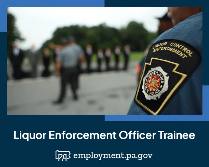 Close up of the Liquor Control Enforcement patch worn on a uniformed officer; in the unfocused background, new Trainees are lined up in front of an instructor on the first day of their training; the words Liquor Enforcement Officer Trainee, the Pennsylvania outline logo, and the URL employment.pa.gov