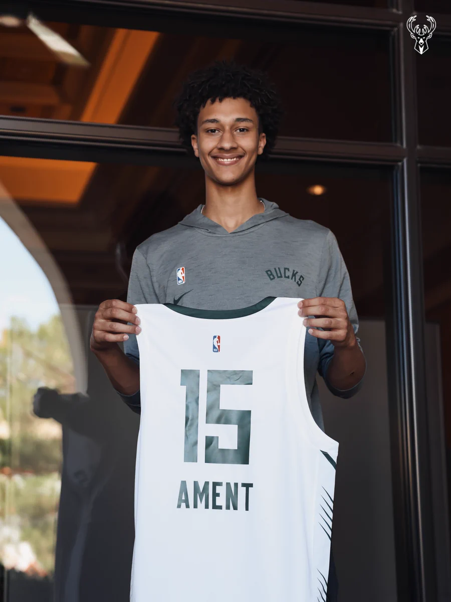 A photo of Nate Ament holding a white Bucks jersey with his last name and number 15 on the back.