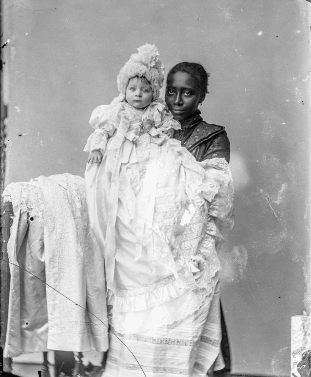 Dr_TheHistories's tweet photo. This remarkable 1903 glass negative captures far more than a woman holding a child. It preserves a glimpse into Peru's complex social hierarchy at the beginning of the 20th Century.

The woman is identified as an ama de leche—literally "milk mother" or wet nurse. Wet nurses were women hired to breastfeed and care for infants whose biological mothers could not or chose not to nurse. The baby is **Isidro Ernesto Ascher Freymann**, the son of a wealthy family, dressed in an elaborate christening gown that sharply contrasts with the practical clothing of the woman holding him.

In Peru, as in much of Europe and Latin America, employing a wet nurse was often a sign of wealth and social status. Elite women sometimes avoided breastfeeding because of health concerns, social expectations, or the belief that nursing would interfere with future pregnancies or their role in high society. Instead, the daily nourishment, and often much of the emotional care, of their infants was entrusted to another woman.

Many Peruvian wet nurses came from Indigenous, Afro-Peruvian, or mixed-race communities. They frequently left their own homes, and sometimes their own babies, to live with affluent families. Some were well compensated by the standards of the day, but others had few economic alternatives. Their labor extended well beyond breastfeeding; many became full-time caregivers, comforting, bathing, dressing, and raising children who were not their own.

The photograph quietly reveals the racial and class divisions that shaped Peruvian society after the abolition of slavery in 1854. Although legally free, many Afro-Peruvian women continued working in domestic service, where opportunities remained limited by entrenched inequality. Wet nursing became one of the few occupations that could provide steady income.

That silence is common in historical photographs. The people whose labor made privileged lives possible were often left unnamed, even when they were central to a child's earliest years. Today, this image stands as a powerful reminder that behind many prominent families were women whose care shaped lives but whose own stories were rarely preserved.

#drthehistories