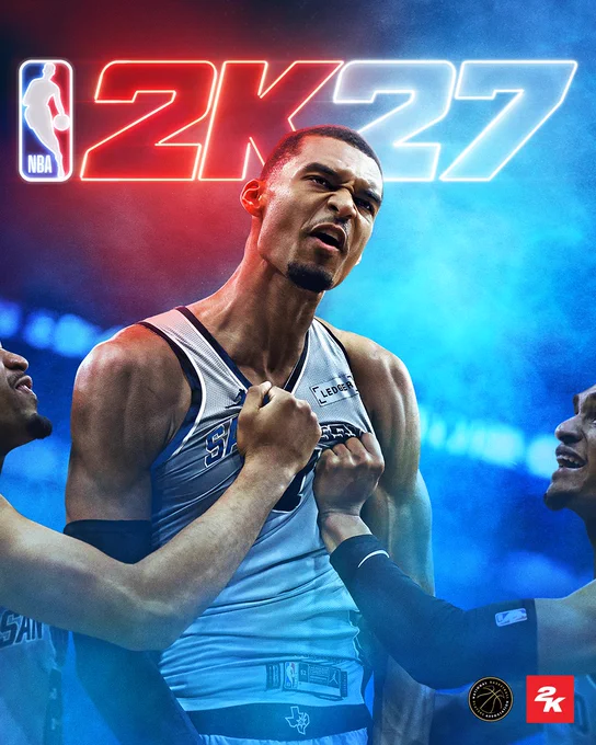 The NBA 2K27 standard cover art. Victor Wembanyama is posed against a blue smoky background. Two teammates' hands are seen grabbing his Spurs jersey as he celebrates.  Above him is a red and white neon "NBA 2K27" logo.