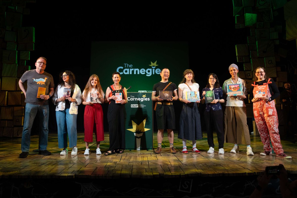 Shortlistees on a stage holding books in front of a backdrop displaying 'The Carnegie' logo.