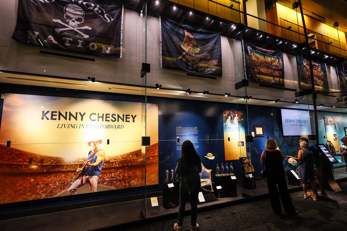 countrymusichof's tweet photo. Last night, the Museum celebrated the opening of "@KennyChesney: Living in Fast Forward," presented by @BlueChairBayRum. The exhibit chronicles Chesney’s path to stardom, from his early years playing in his university’s bluegrass band to becoming one of the top touring acts of this century. The exhibit includes instruments, memorabilia, manuscripts, awards, photographs, and more.
 
Get tickets: https://t.co/q3otc8iKSm