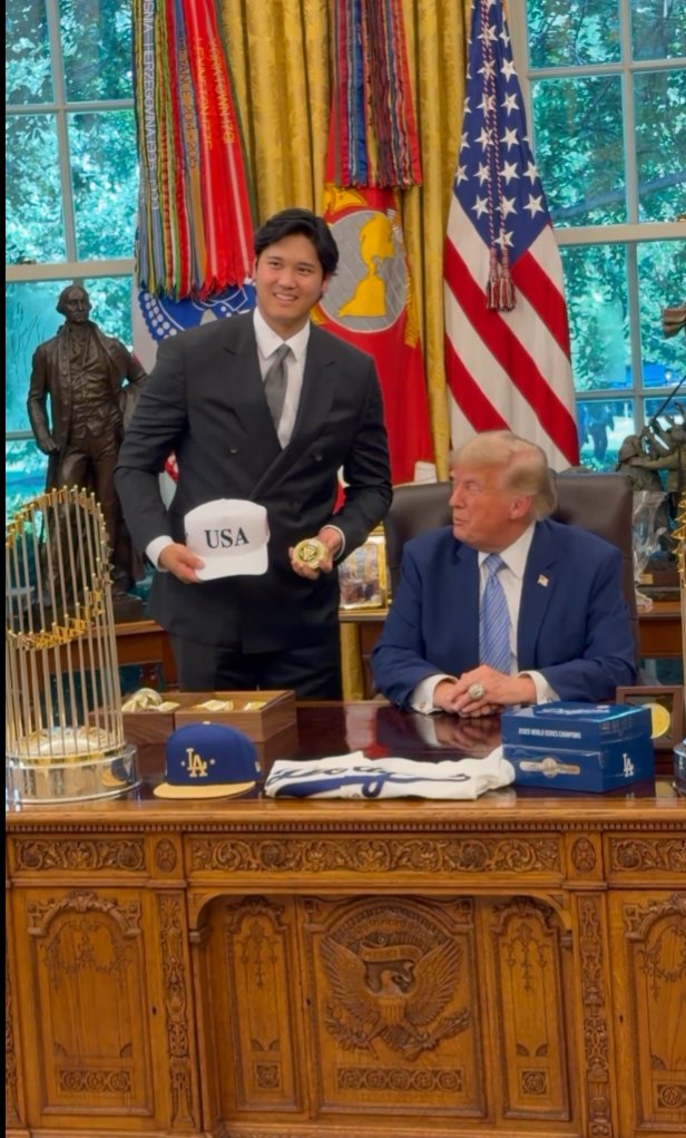 naoyafujiwara's tweet photo. Claudeが教えてくれました

大谷翔平がトランプからもらったPresidential Challenge Coinとは？

－＞軍のメダルよ。日本人の大谷が米軍のメダルをもらったんだよ！大谷が軍事作戦で立派に活躍したというわけでしょう

Presidential Challenge Coin(大統領チャレンジコイン)は、アメリカ合衆国大統領が自らの名で発行する記念メダルで、軍の伝統である「チャレンジコイン」文化の頂点に位置するものです。

まず土台となるチャレンジコインの伝統から説明すると、これは米軍の部隊やコマンドが独自のデザインで作る金属製の記念コインで、部隊章やモットーが刻まれ、隊員であることの証や士気高揚のために配られます。起源には諸説あり、第一次大戦で撃墜された米飛行士が部隊のコインで身元を証明し処刑を免れたという有名な逸話がありますが、史実としては朝鮮戦争からベトナム戦争期に特殊部隊などで広まった慣行と見るのが有力です。名前の由来は酒場での「チャレンジ」の儀式で、誰かがコインをテーブルに叩きつけたら全員が自分のコインを提示せねばならず、出せなかった者が全員に酒をおごる、というルールに因みます。

この軍の文化を大統領府に持ち込んだのがビル・クリントンで、1990年代半ばに大統領として初めて公式のチャレンジコインを作りました。以来、歴代大統領がそれぞれ独自のデザインのコインを持つことが慣例となっています。意匠は基本的に大統領章と本人の名前・署名を組み合わせたもので、製作は大統領府軍事室(White House Military Office)系統の組織が担います。クリントンが執務室に集めたコインのコレクションは、彼の公式肖像画の背景にも描き込まれています。

使われ方に独特の作法があります。大統領が基地訪問などで兵士と握手する際、手のひらにコインを忍ばせてそっと渡す「シークレット・ハンドシェイク」が定番で、受け取った兵士にとっては最高位の栄誉とされます。また外国要人への贈答品、ホワイトハウス訪問者への記念品としても使われ、大統領専用機や海兵隊ヘリの乗務員、シークレットサービスまで、大統領周辺の組織がそれぞれ自前のコインを持っています。副大統領、閣僚、統合参謀本部議長、議員に至るまでこの文化は広がっており、ワシントンでは一種の名刺代わり、権威と人脈の象徴として機能しています。収集市場も存在し、大統領コインは特に人気の高いジャンルです。

政治的な話題になったこともあります。トランプ政権の2017年版コインは、伝統の国是「E Pluribus Unum(多数から一つへ)」を選挙スローガン「Make America Great Again」に置き換え、金色を基調に自身の名を三か所に刻んだ派手な意匠で、伝統からの逸脱だと論争になりました。2018年の米朝首脳会談に先立って大統領府通信局が作った記念コインは、会談実現前に金正恩を「最高指導者」として肖像化したことが批判を浴び、直後に会談中止騒動が起きたため皮肉の的にもなりました。バイデンは伝統的な意匠に戻し、亡き息子ボーが所属したデラウェア州兵部隊への追悼をあしらったコインを作っています。

要するにこれは、軍隊の仲間内の記念品文化が最高司令官たる大統領の権威と結びつき、栄誉の授与、外交儀礼、そして時に政治的自己演出の道具にまでなったもの、と位置づけられます。硬貨(通貨)ではなくあくまで記念メダルであり、法定通貨としての価値は持たない点も付け加えておきます。