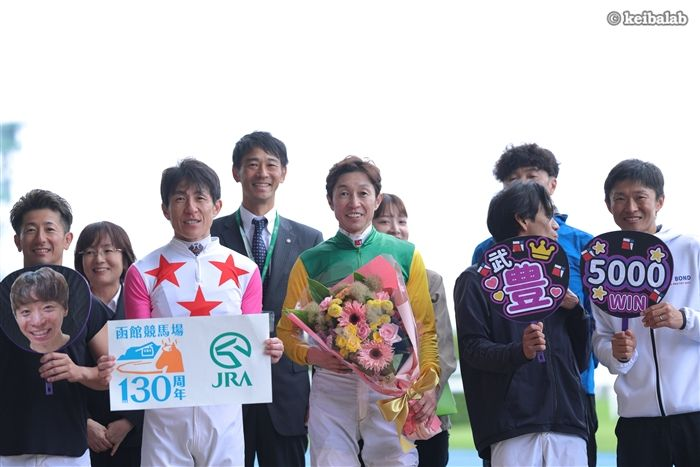 keibalab's tweet photo. 【遠隔参加】
こちらは武豊騎手のJRA、地方、海外合計5000勝の記念セレモニーの様子。

武豊騎手の大ファンでお馴染み・池添謙一騎手は本日七夕賞のサヴォーナに騎乗するため福島競馬場へ。不在のため顔写真入りうちわでの参加となりました。
#武豊 #池添謙一
https://t.co/N4OWFzNYLi https://t.co/TQUB4HvEwR