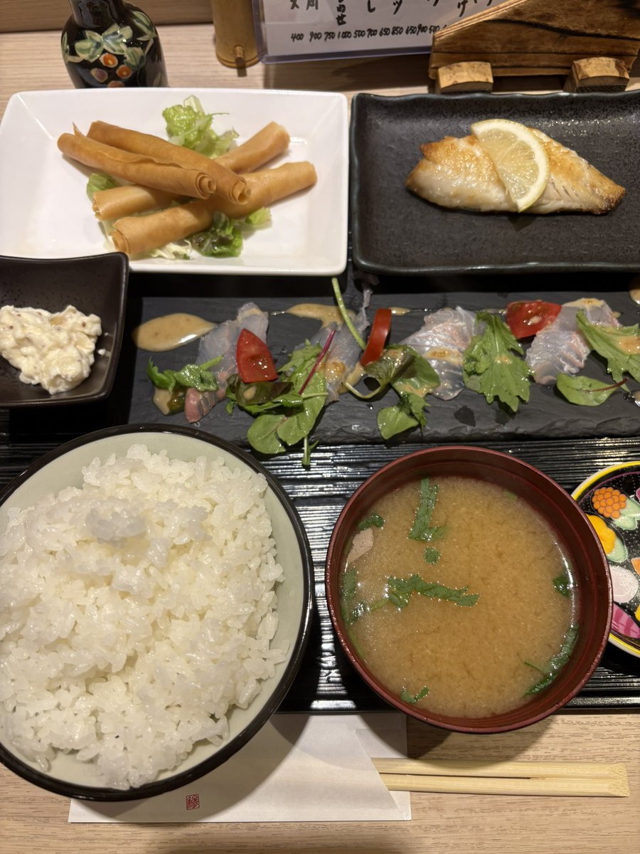 LunchTime_Quest's tweet photo. 本日乃昼餉😋

『黒さわ』@荒川区 日暮里
本日の日替り定食　¥990

・板盛り（カルパッチョ風）
・赤魚塩焼き
・海老チーズ春巻き

今日の板盛りはカルパッチョ風✨
しっとりとした白身に
香ばしい胡麻ダレがよく絡み、
彩り豊かな野菜と一緒に
さっぱりいただける一皿😋

赤魚の塩焼きは皮目が香ばしく、
身はふっくら☺️
程よく脂が乗り、レモンを搾れば
素材の旨みがさらに引き立つ✨

海老チーズ春巻きは､
パリッと軽快な皮の中から、
ぷりっとした海老とチーズの旨味❗️
揚げ物ながら重たさはなく、
ご飯がどんどん進む旨さ😋

これだけの品数と満足感で¥990❗️
今日も隙のない日替り定食に
大満足、ごちそうさまでした☺️